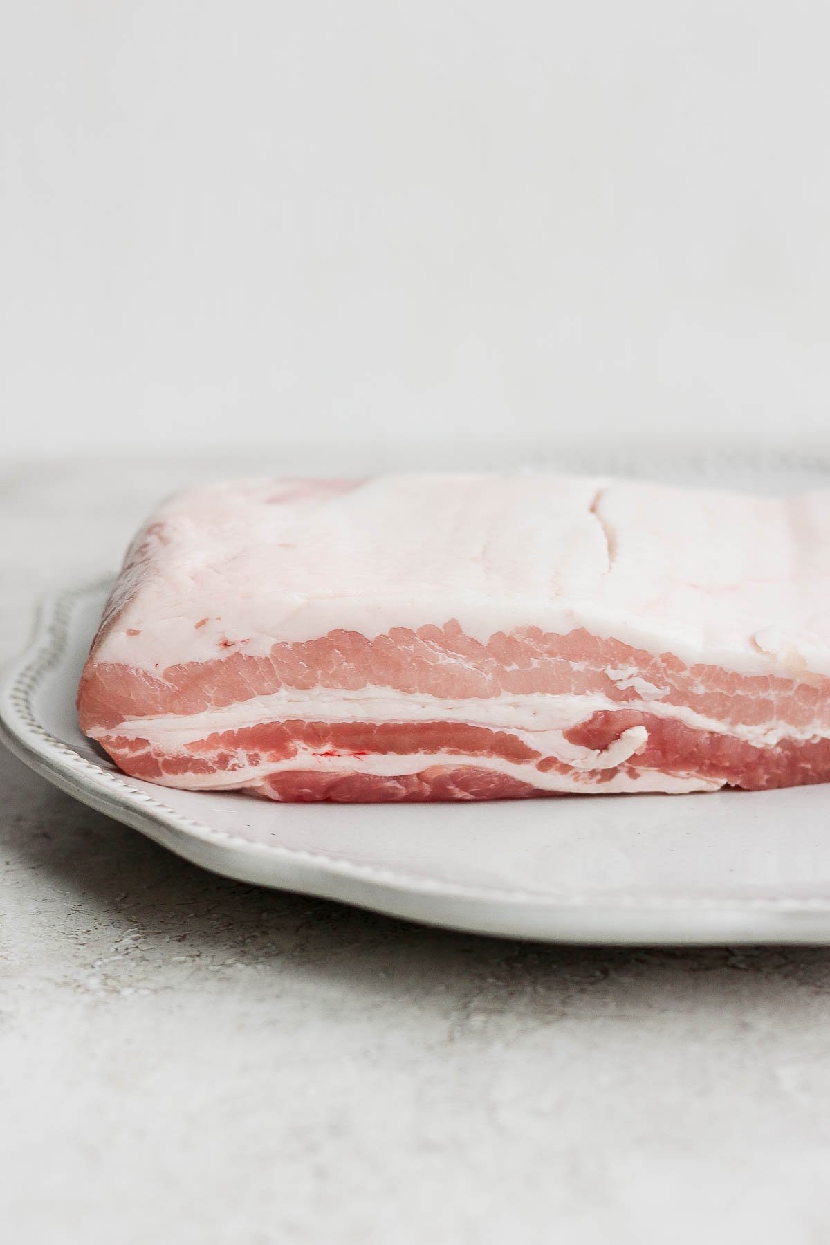 A piece of raw pork belly sitting on a plate. 