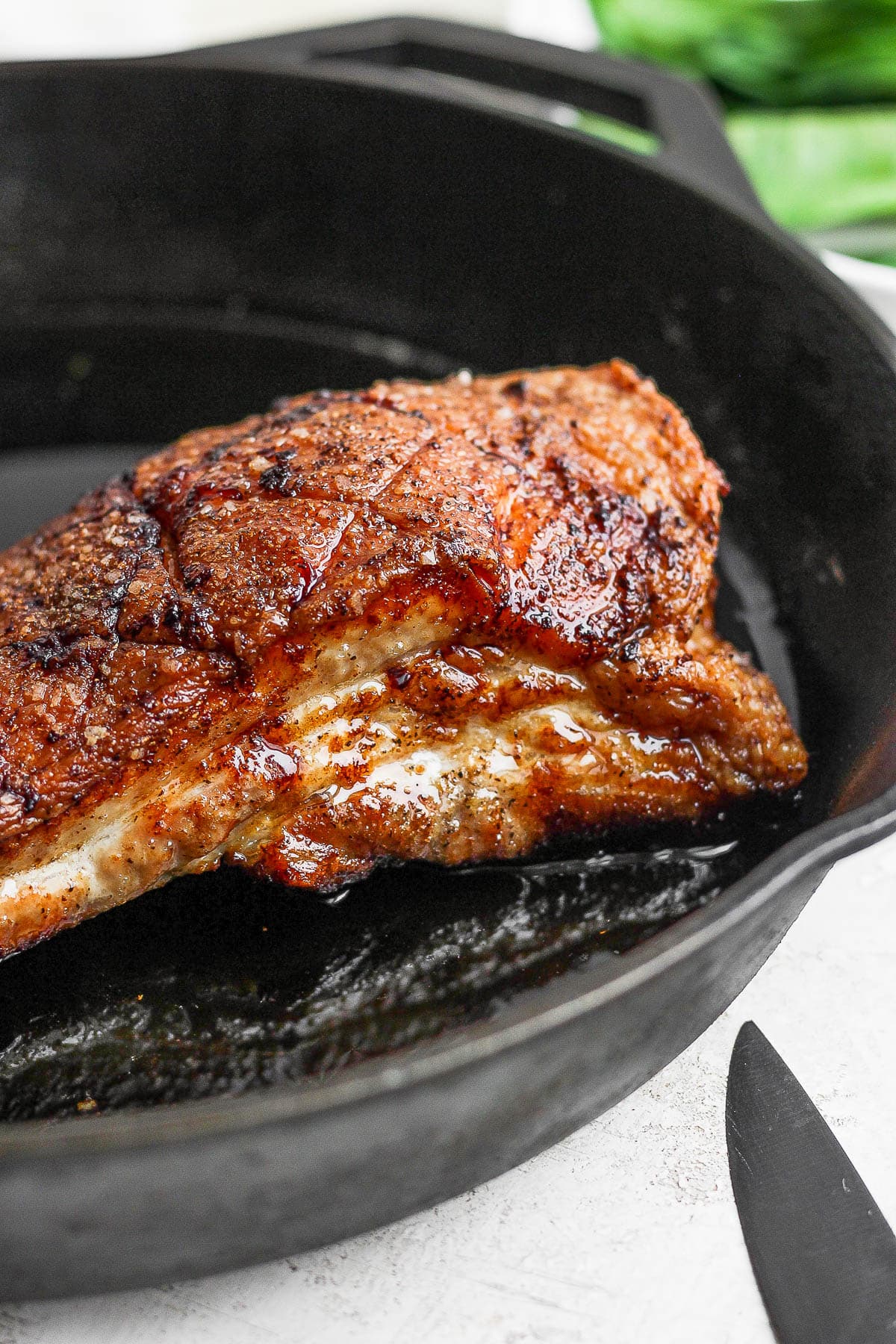 A piece of pork belly sitting in a cast iron skillet, cooked and crispy. 