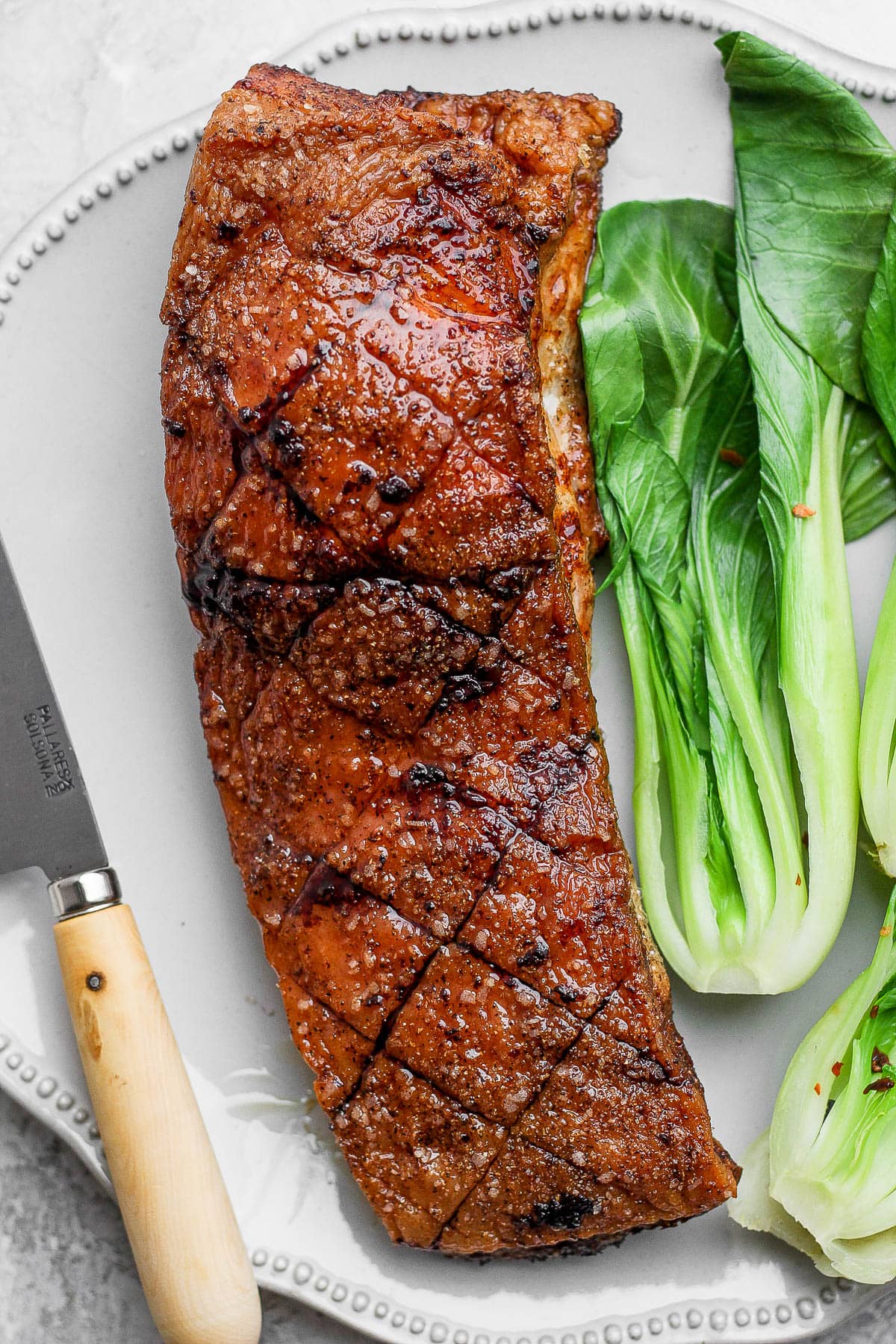 A piece of cooked pork belly on a large plate with some bok choy. 