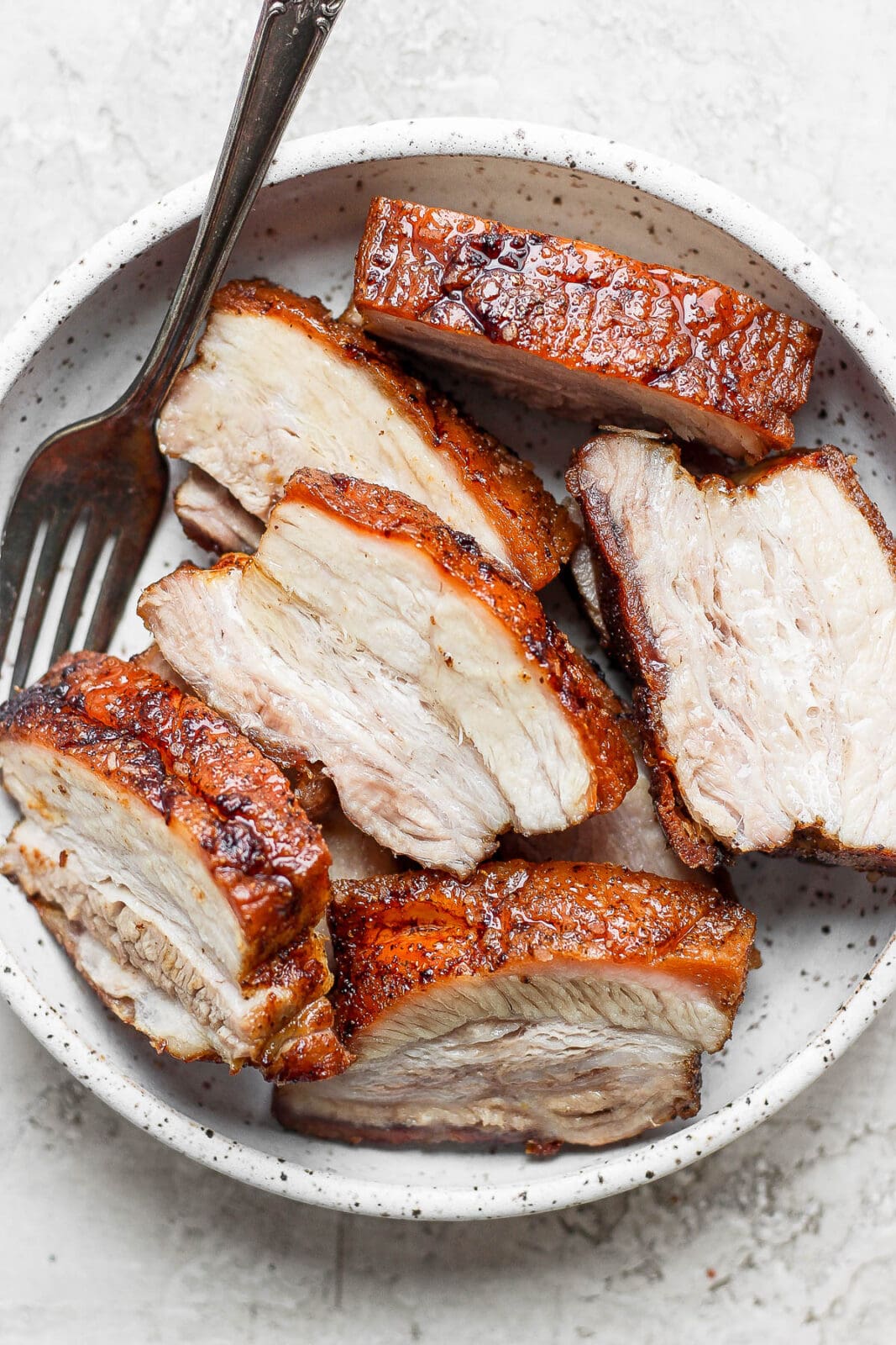 Pieces of cooked pork belly, cut into slices, in a shallow bowl. 