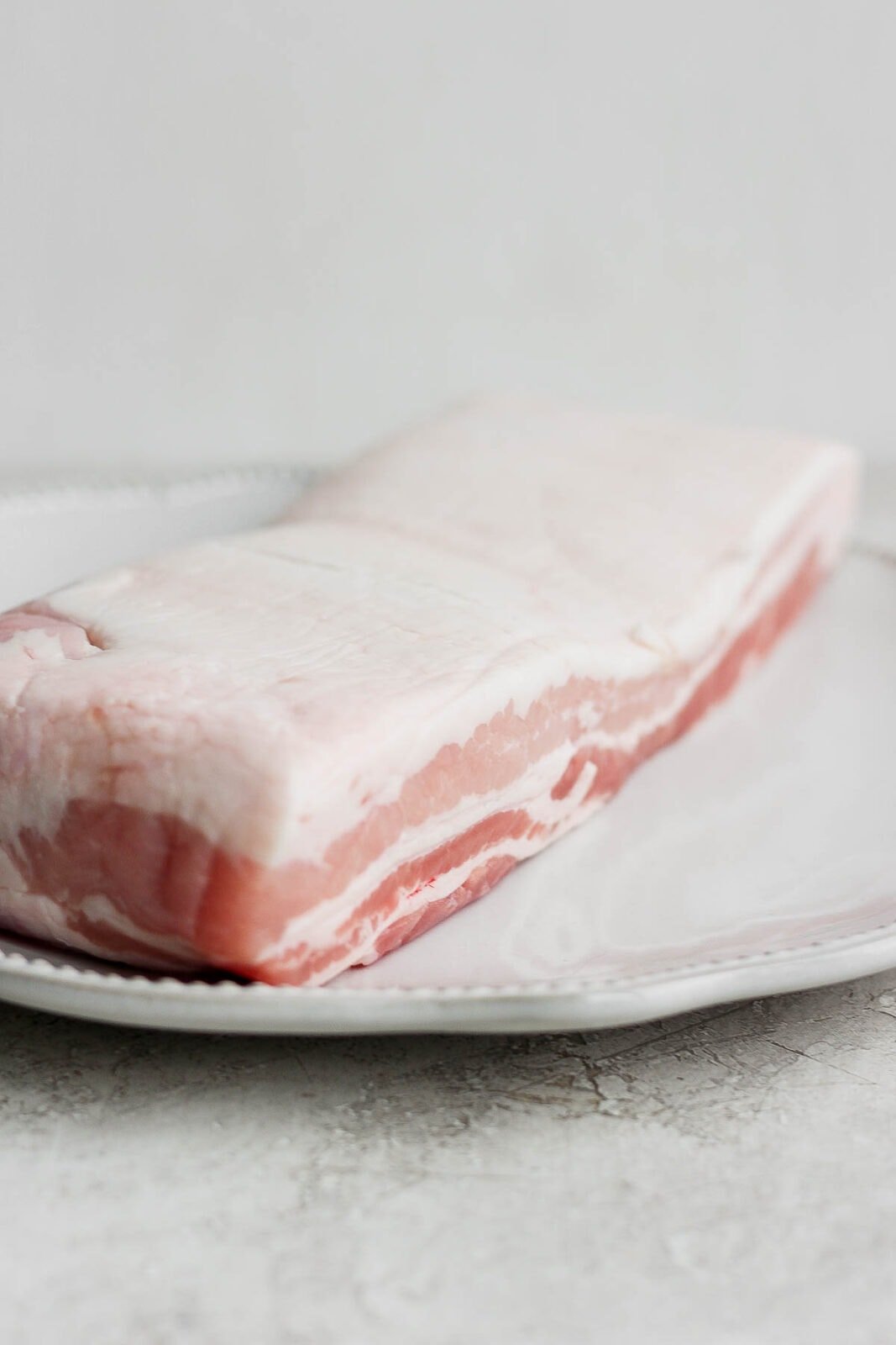 A piece of raw pork belly sitting on a plate. 