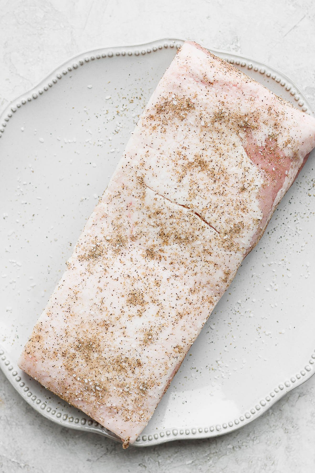 A piece of raw pork belly sitting on a plate covered in some seasoning.