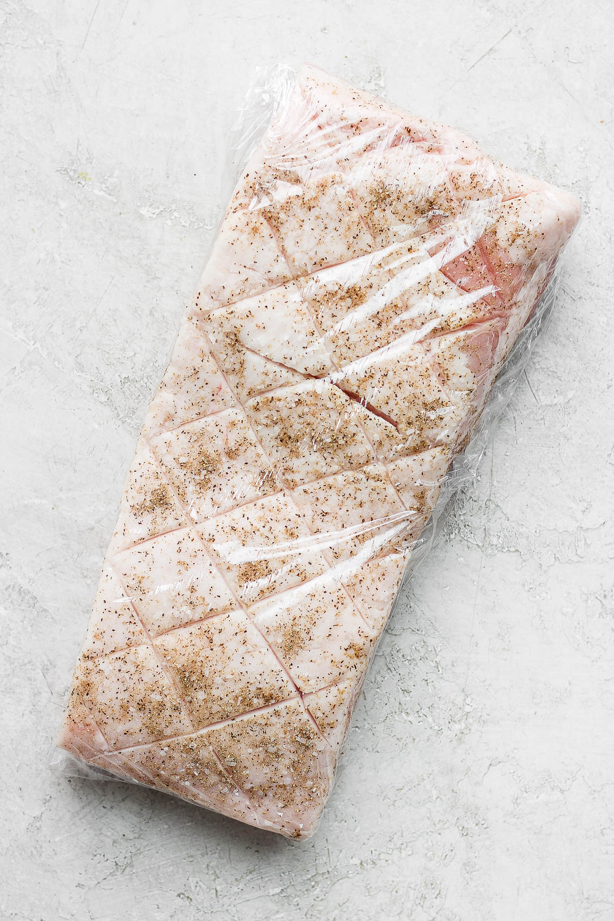 A piece of pork belly scored, rubbed with seasoning and wrapped plastic wrap. 