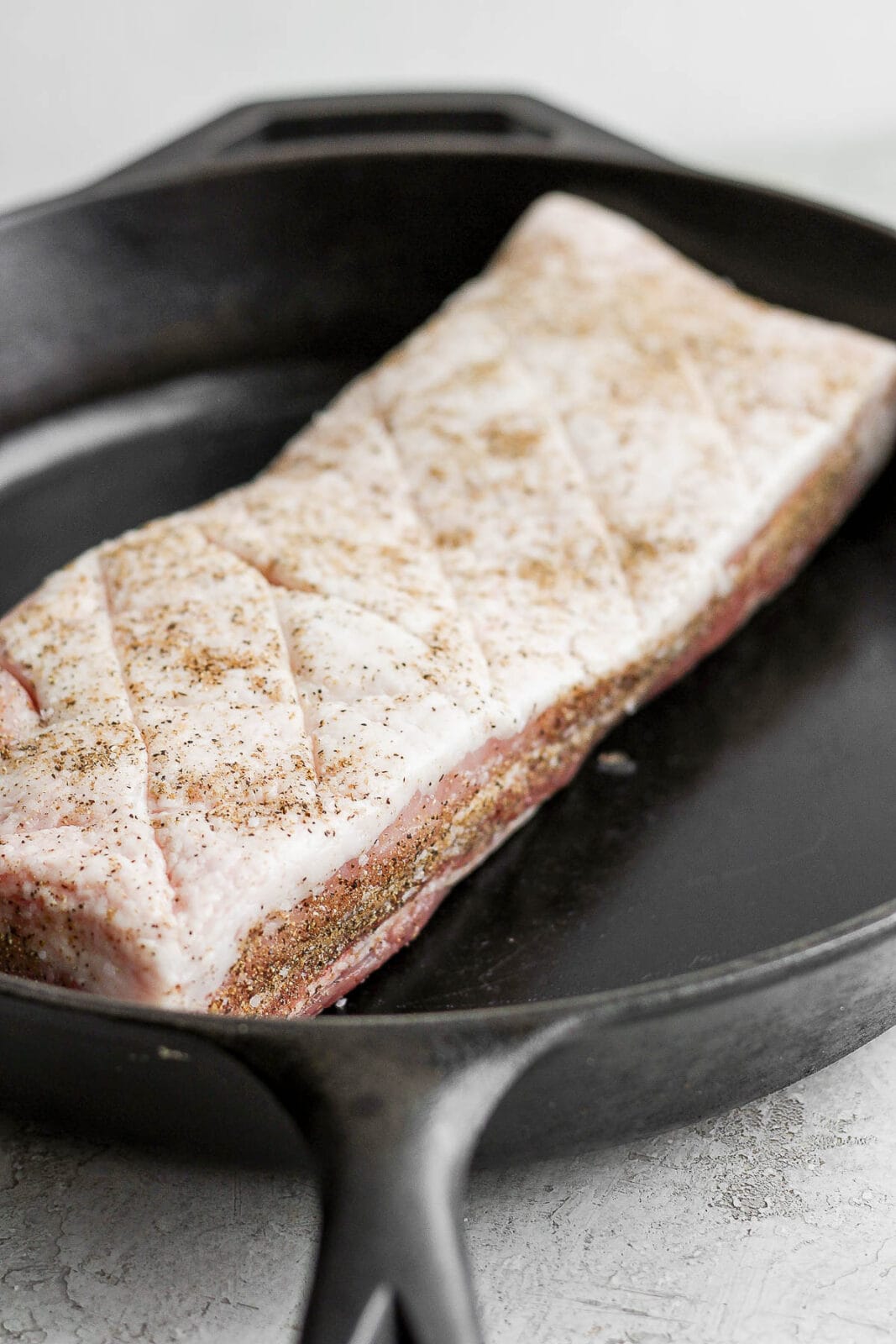 A piece of raw pork belly sitting on a cast iron skillet. 