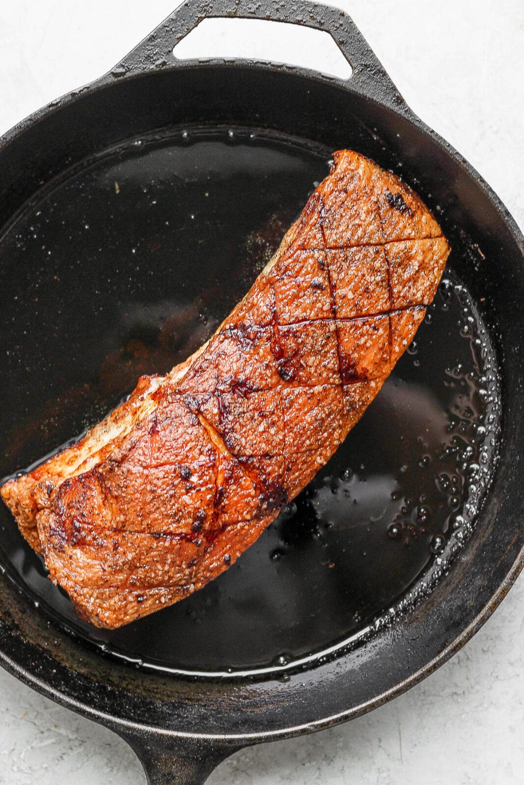 A piece of cooked pork belly in a cast iron skillet. 
