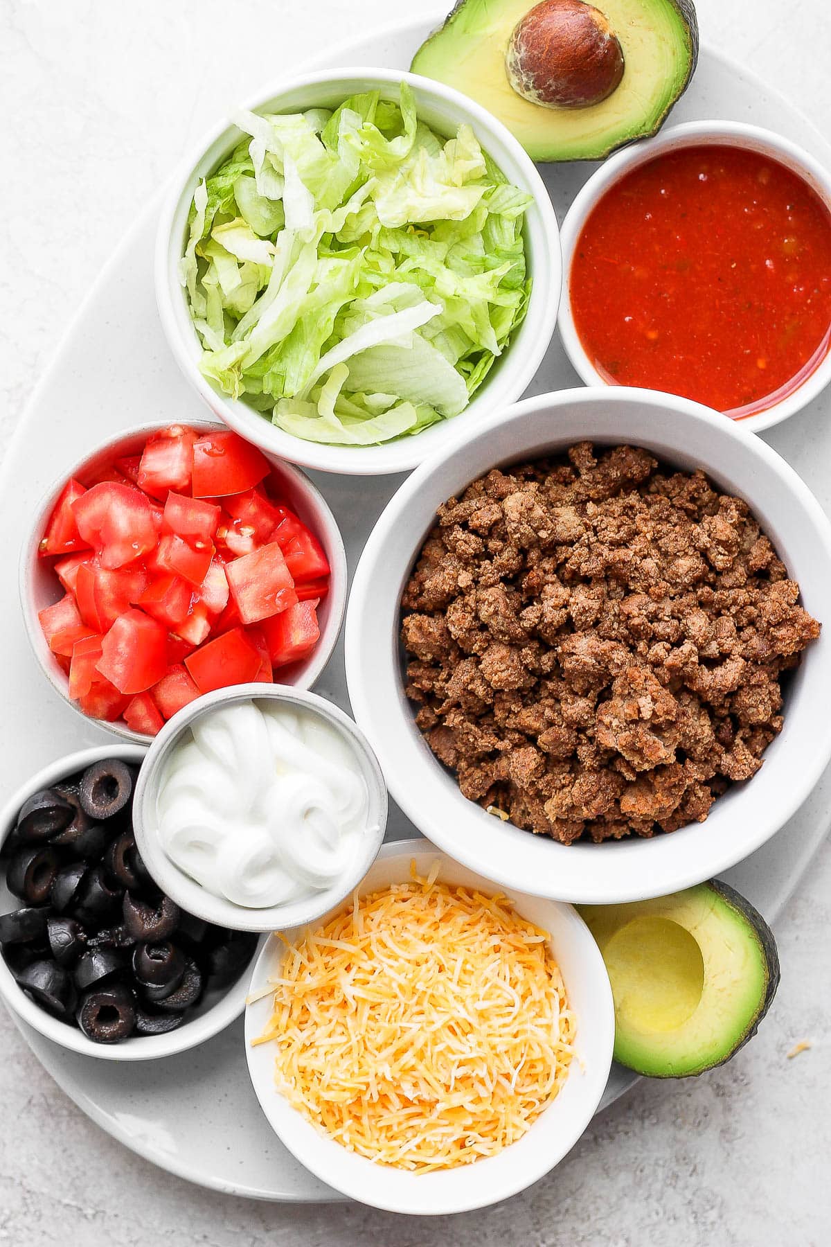 Large plate with several small bowls that each hold a different ingredient for tacos included cooked taco meat.