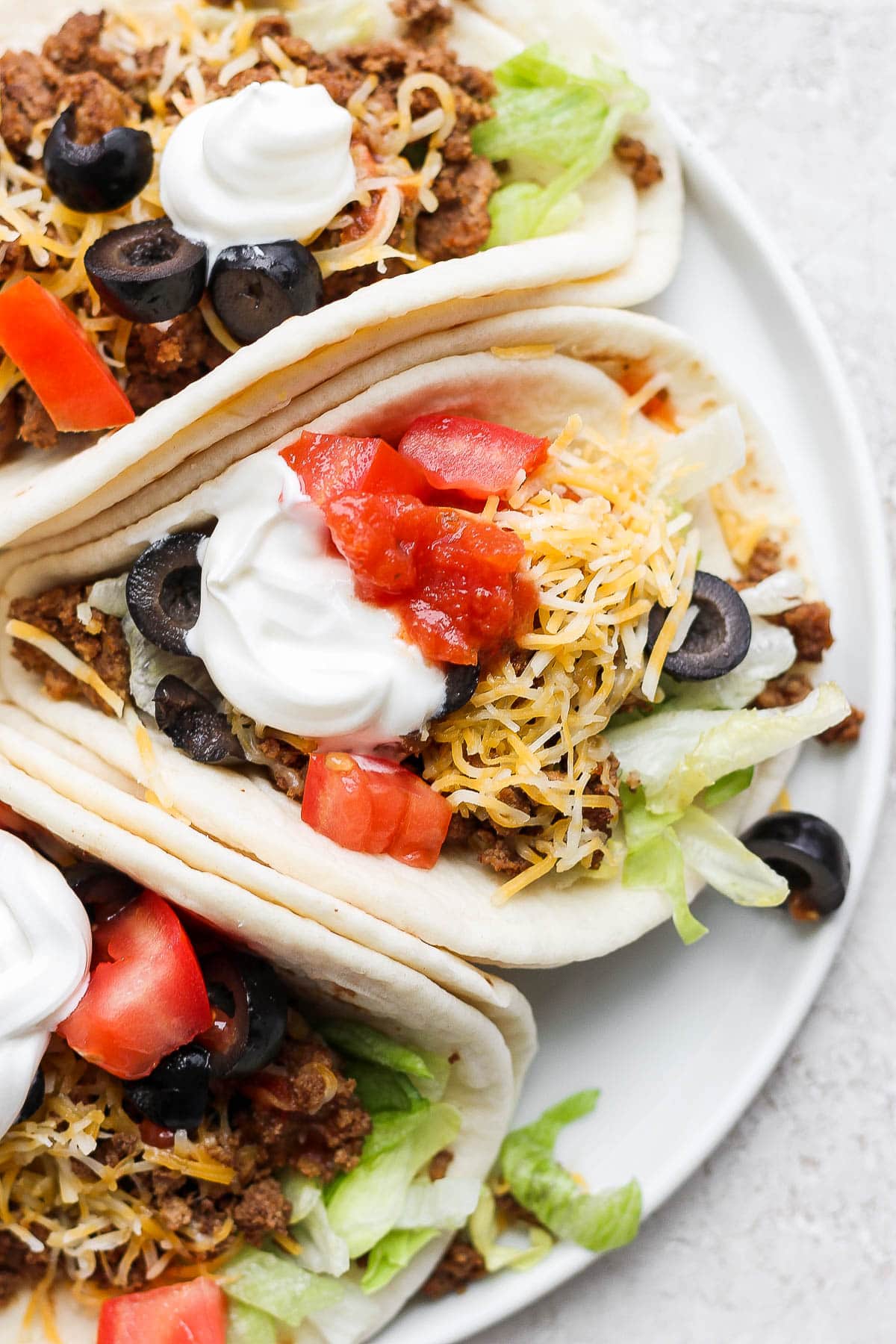 A plate with 3 homemade tacos in soft shell tortillas.