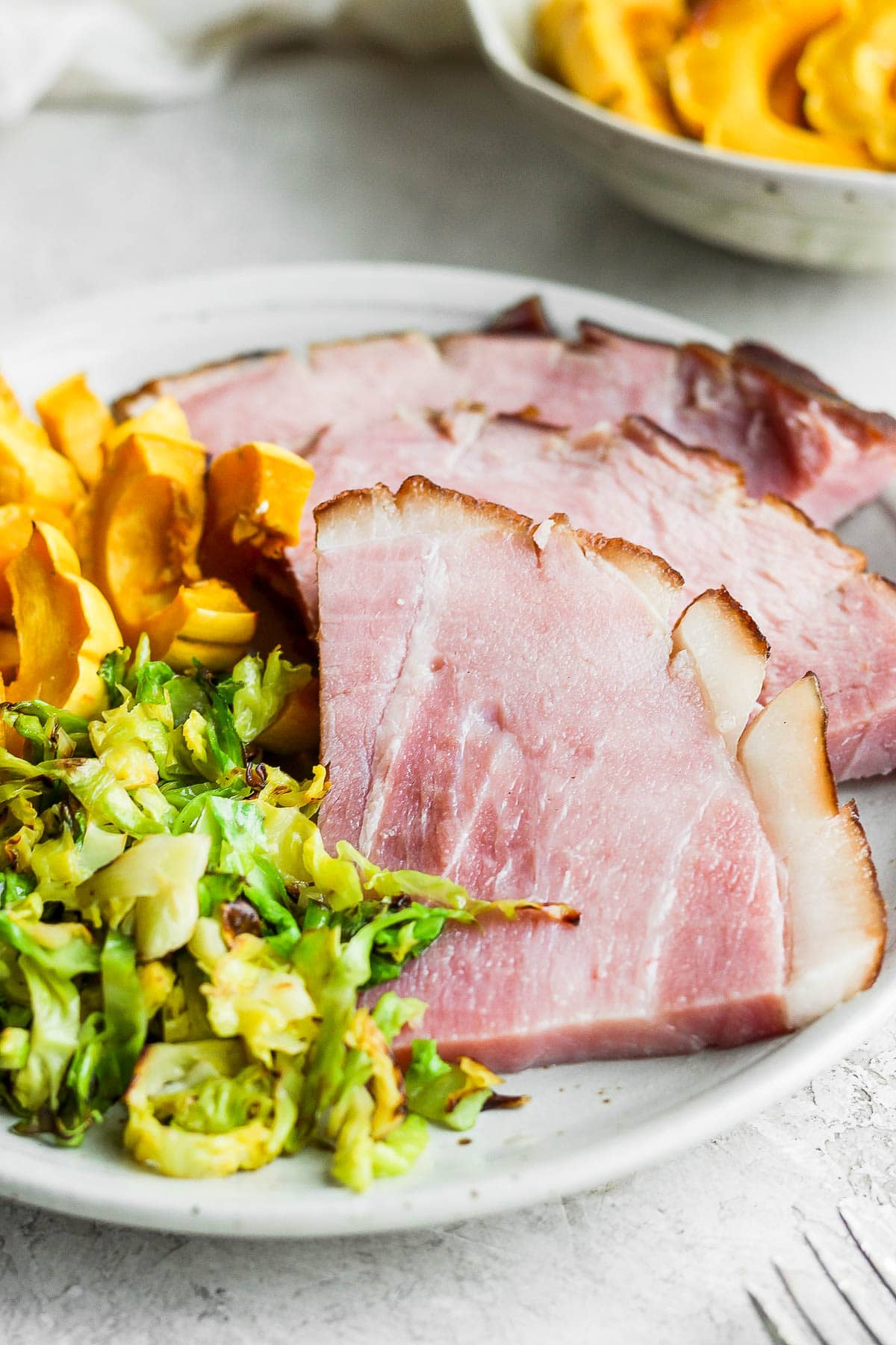 Plate with slices of baked ham, squash, and shaved brussel sprouts.