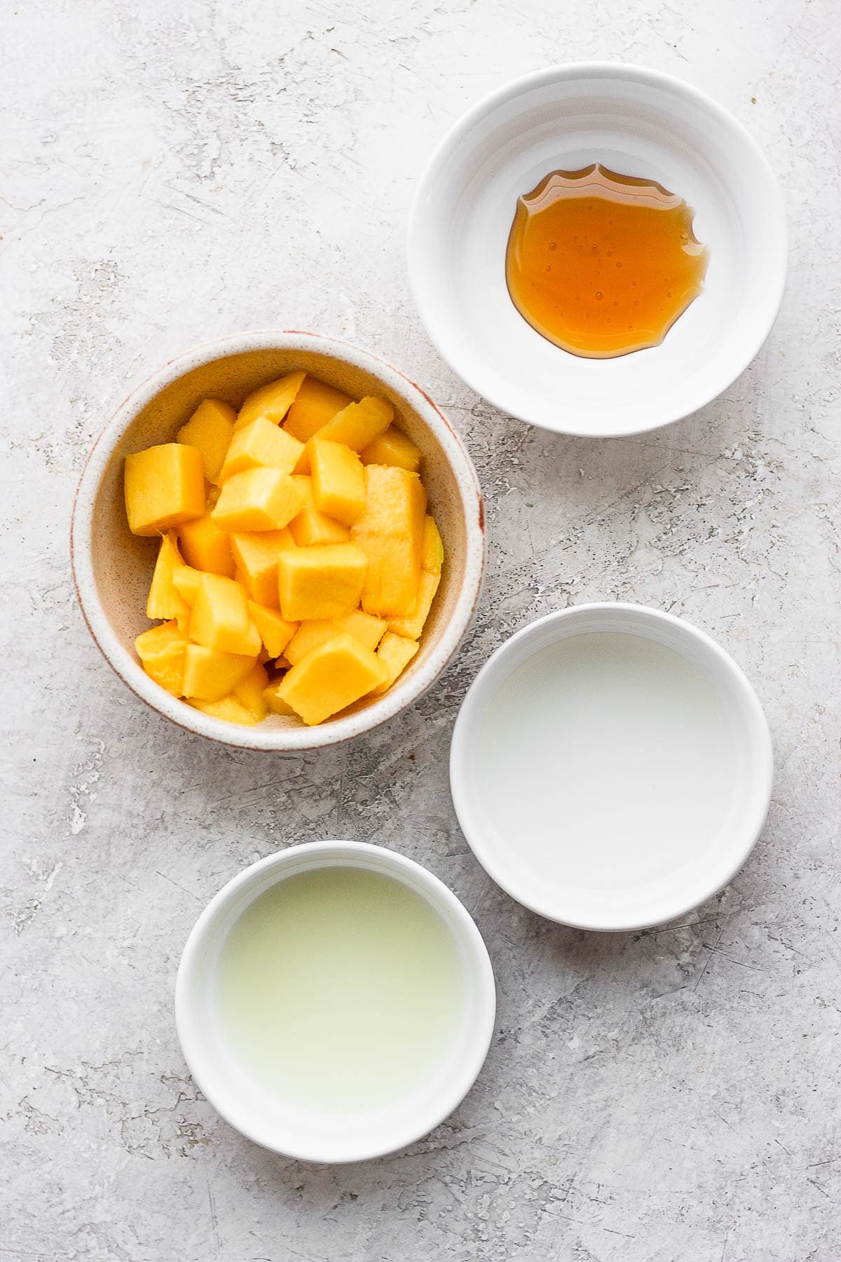 Ingredients for mango margaritas in small white bowls. 