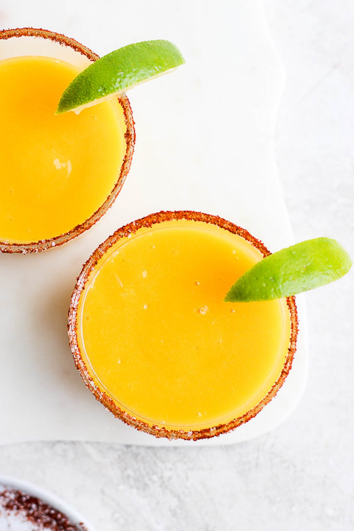 Mango Margarita in a glass with a chili lime rim and fresh lime. 