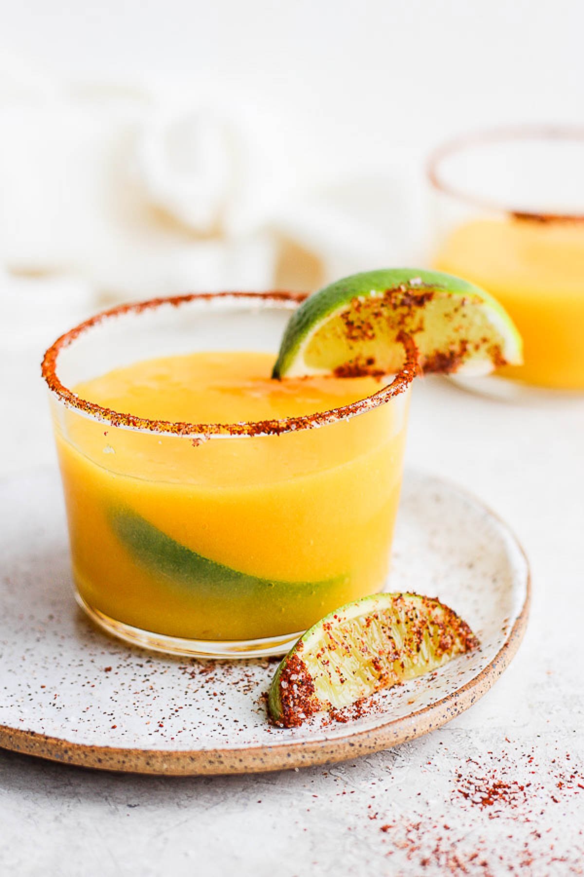 Mango Margarita in a glass with a chili lime rim and fresh lime. 