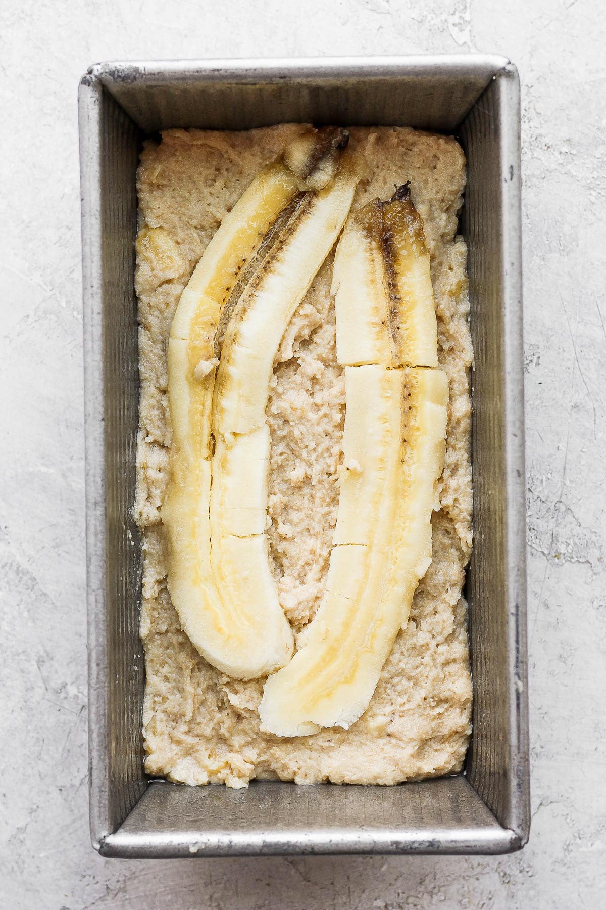 Paleo banana bread batter with a sliced banana on top for garnish in a loaf pan.