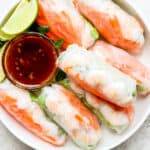A shallow bowl filled with shrimp spring rolls with a small bowl of dipping sauce and a few lime wedges.