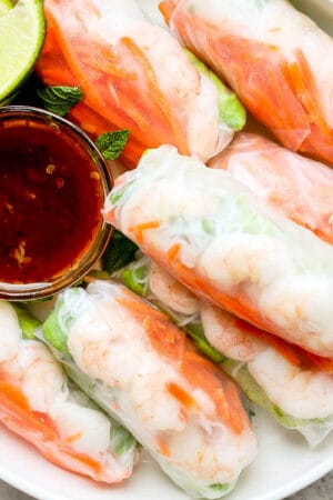 A shallow bowl filled with shrimp spring rolls with a small bowl of dipping sauce and a few lime wedges.