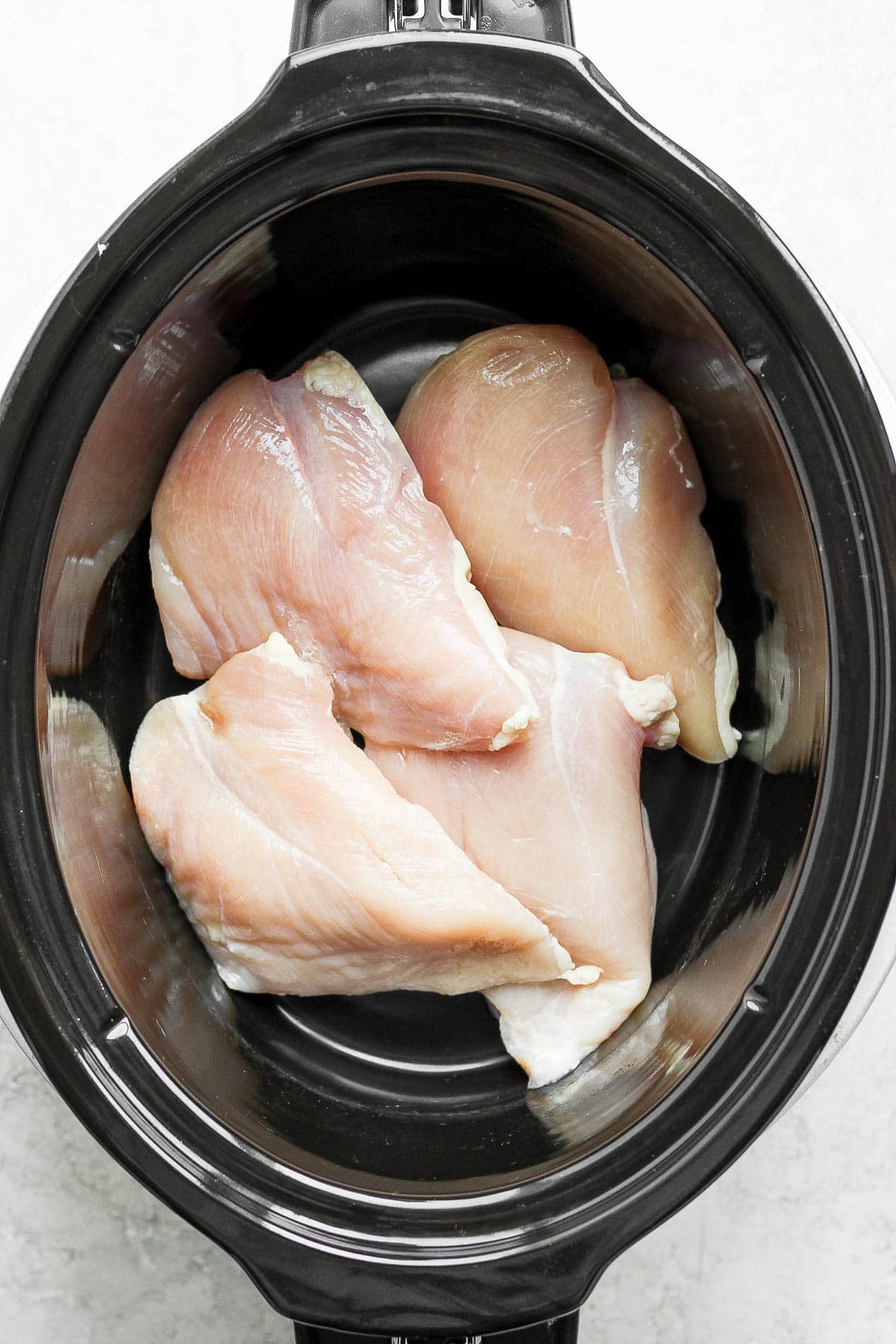 4 raw chicken breasts in a slow cooker.