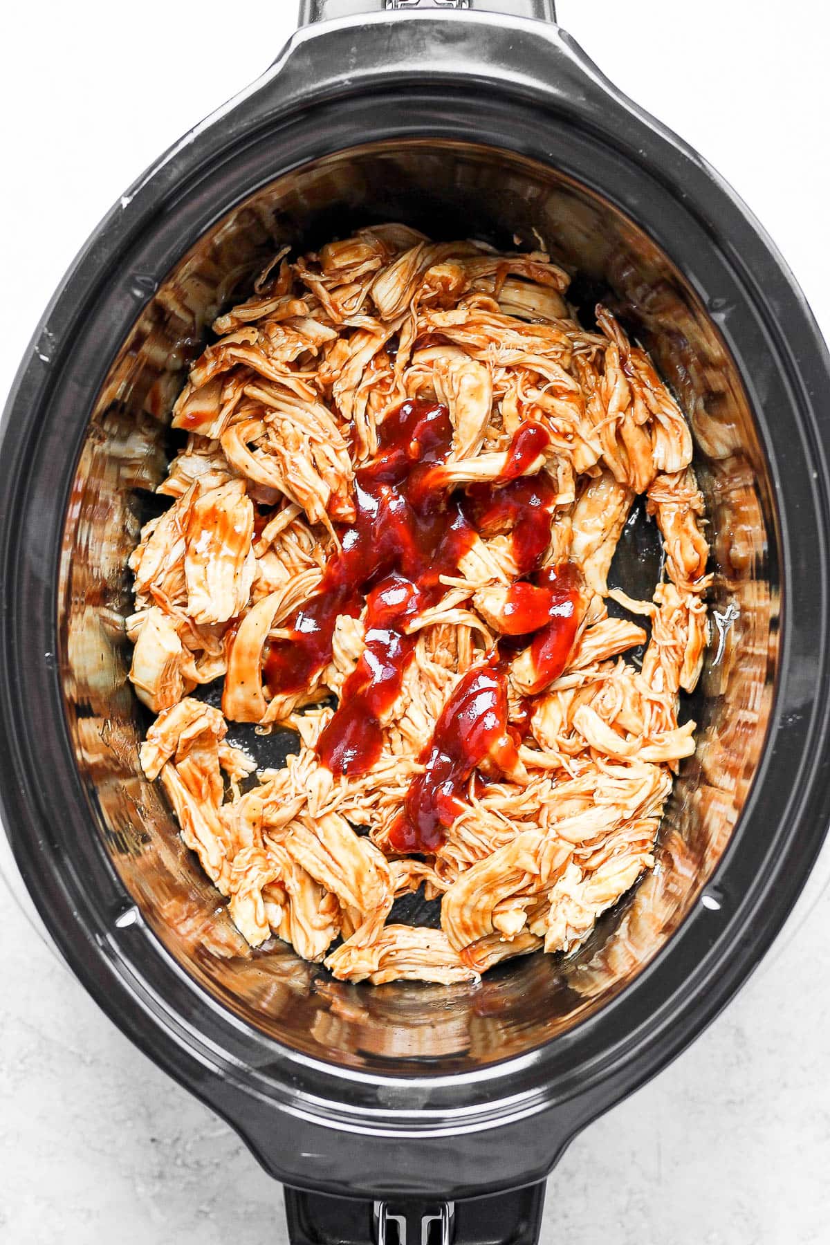 Cooked, shredded chicken in a slow cooker with BBQ sauce.