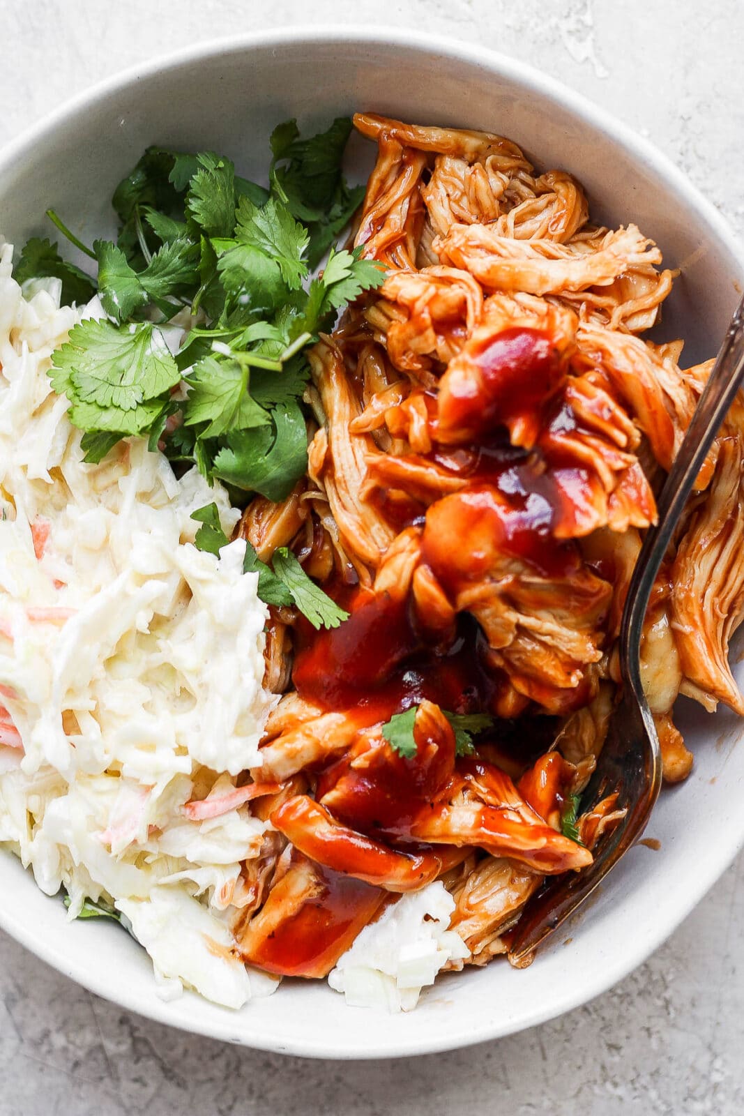 Crockpot BBQ chicken in a bowl with coleslaw and cilantro.