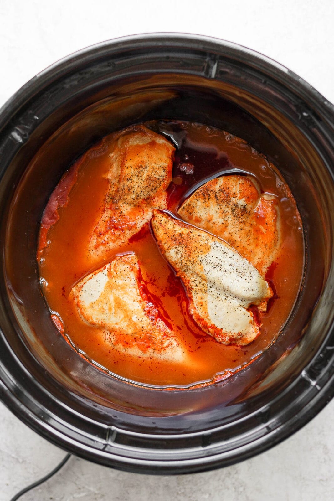 Slow cooker with cooked breasts in buffalo sauce.