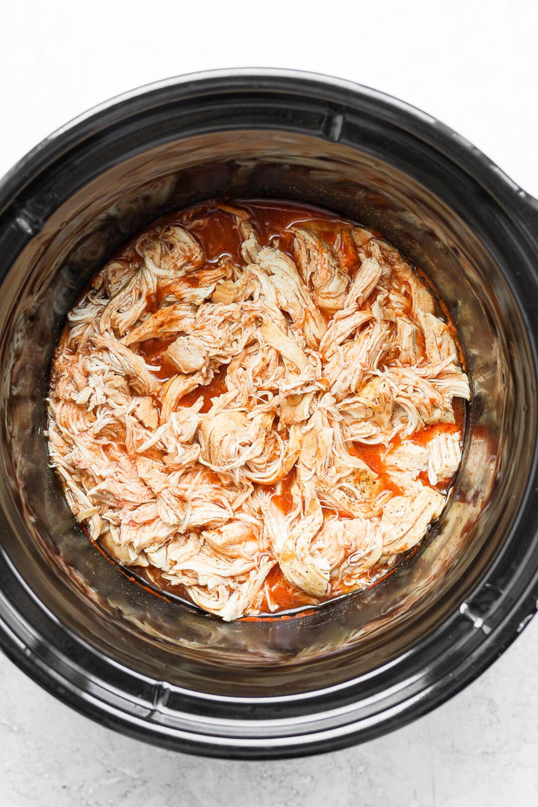 Slow cooker with shredded chicken and buffalo sauce.