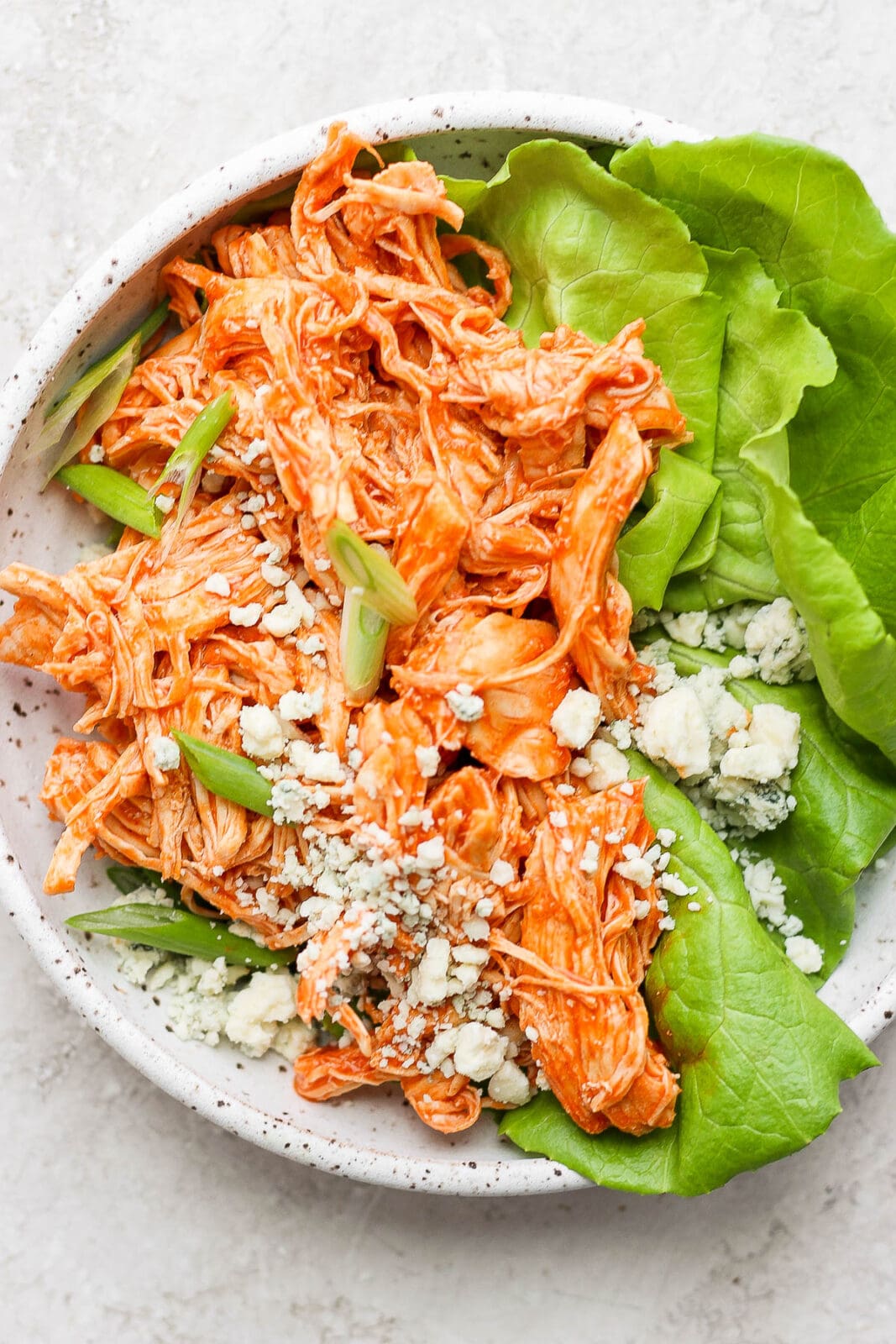 Plate with shredded buffalo chicken on butter lettuce with green onions and blue cheese crumbles.