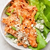 Slow cooker buffalo chicken on a shallow plate with lettuce and blue cheese crumbles.