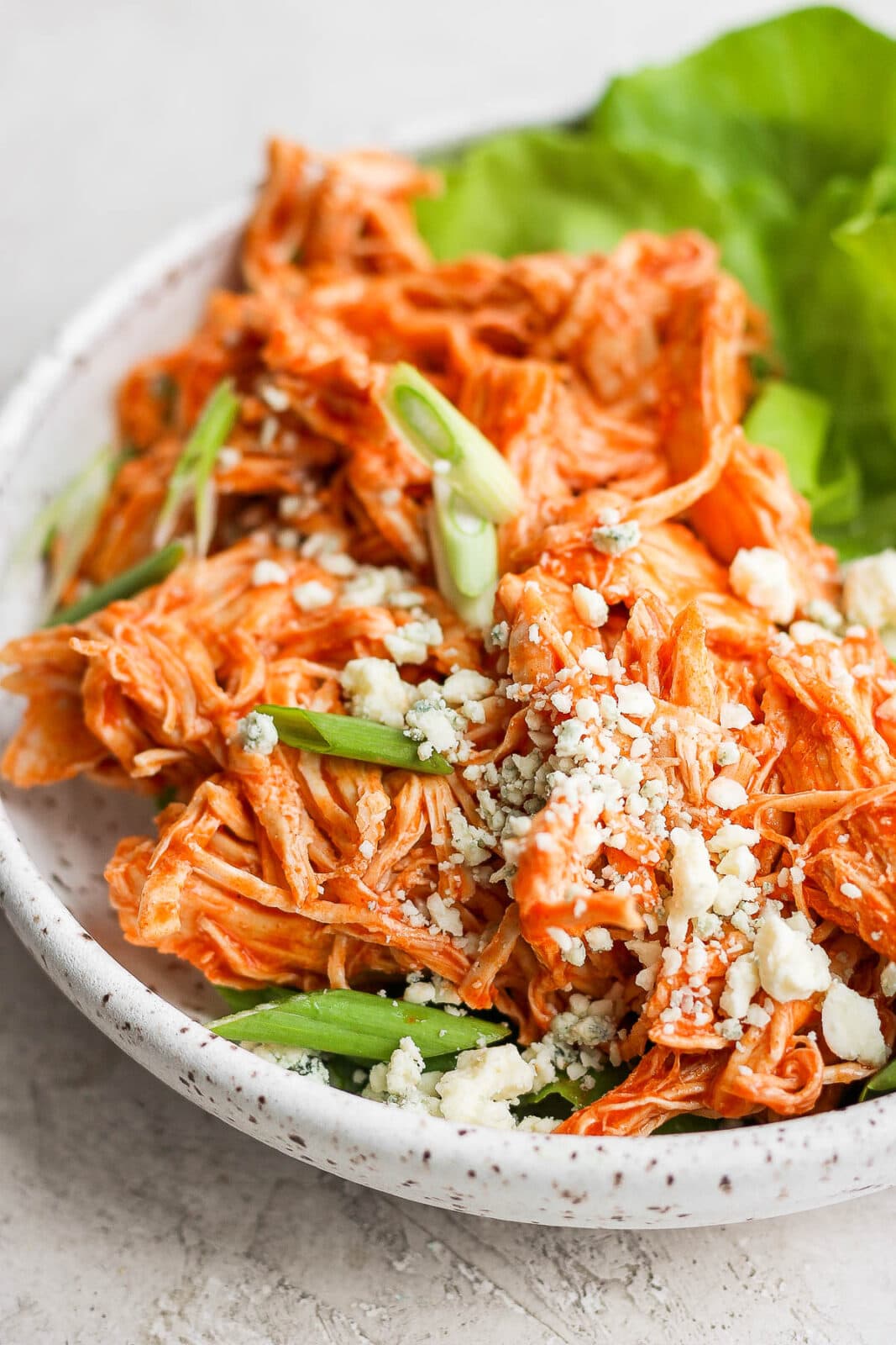 Plate of shredded buffalo chicken on butter lettuce with green onions and blue cheese crumbles.