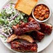 A plate of smoked baby back ribs, coleslaw, cornbread and baked beans.