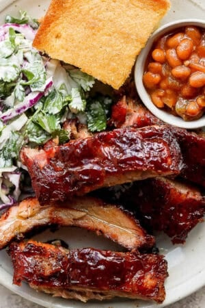 A plate of smoked baby back ribs, coleslaw, cornbread and baked beans.