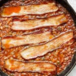 Top downs shot of cast iron skillet filled with smoked baked beans and bacon on top.