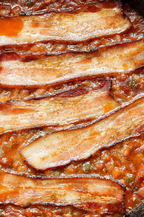 Top downs shot of cast iron skillet filled with smoked baked beans and bacon on top.