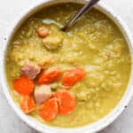 A bowl of split pea soup with ham with a spoon sticking out.