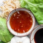A small bowl of spring roll dipping sauce next to some lettuce, avocado, garlic, and soy sauce.