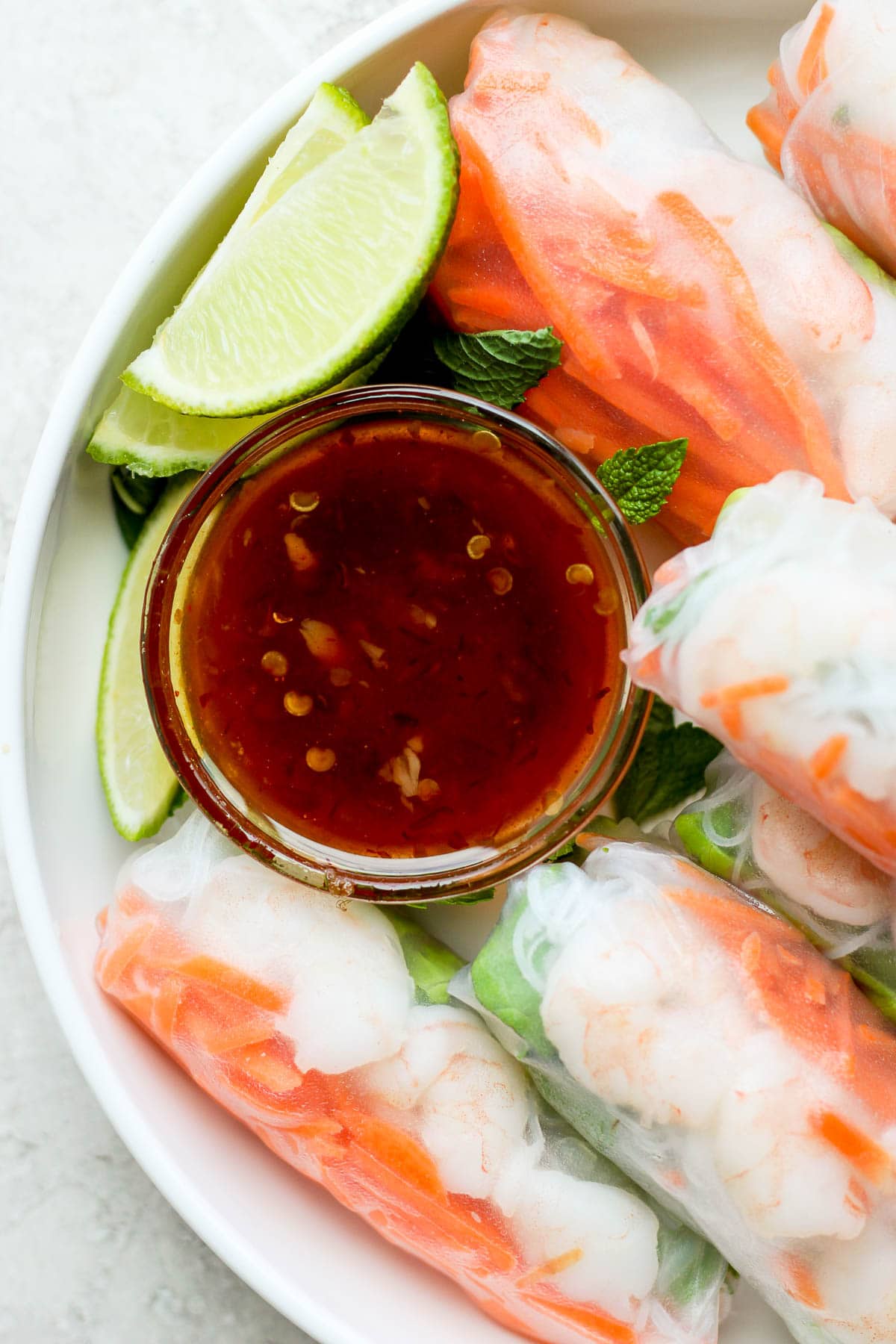 Spring roll dipping sauce in a small dish surrounded by fresh shrimp spring rolls.