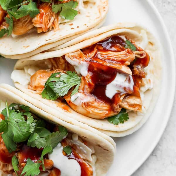Three bbq chicken tacos on a plate with cilantro and ranch dressing.