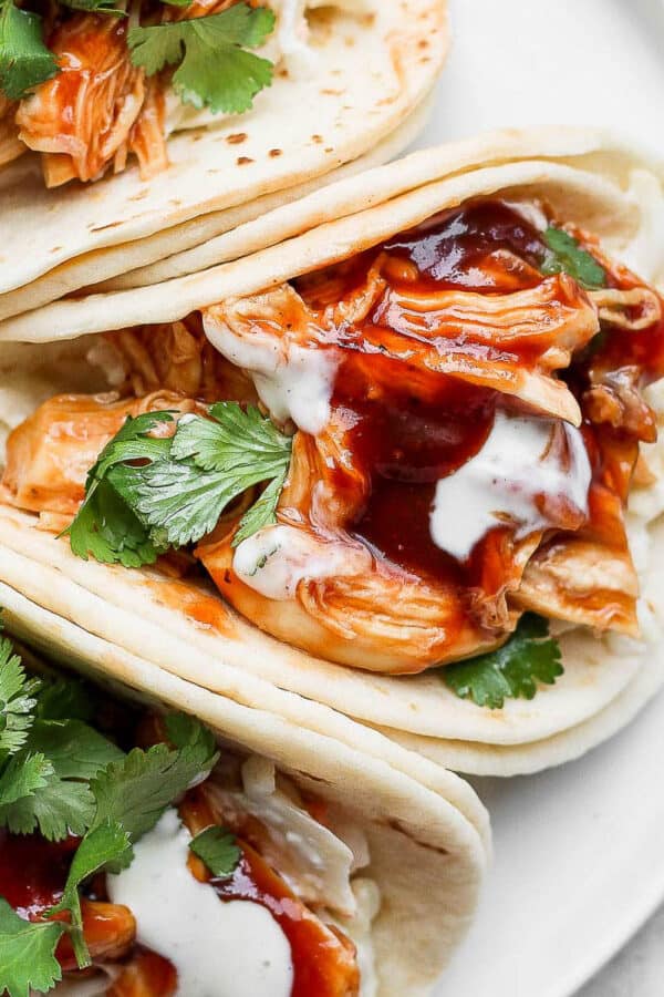 Three bbq chicken tacos on a plate with cilantro and ranch dressing.