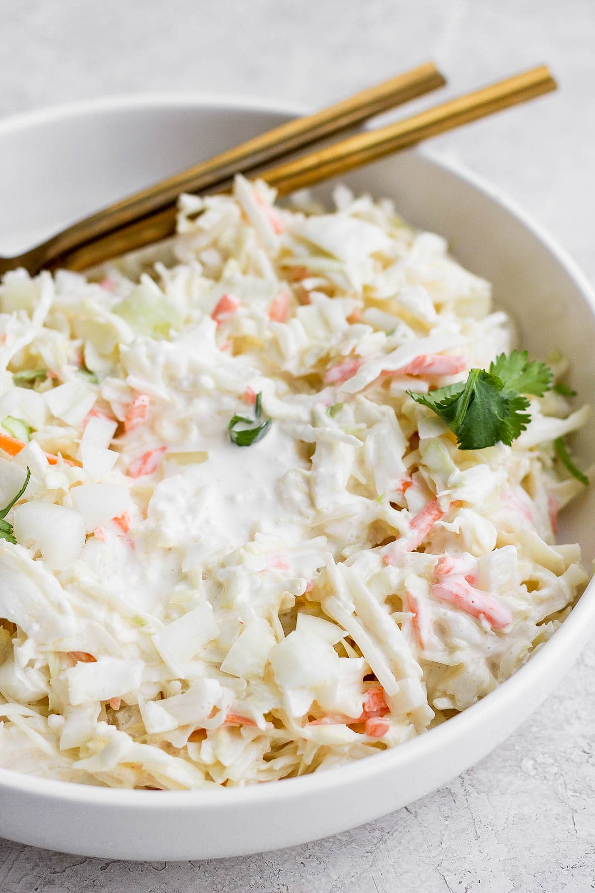 A bowl of creamy coleslaw with 2 spoons.