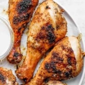 Close-up image of two grilled chicken legs on a plate with a small dish of dip off to the side.
