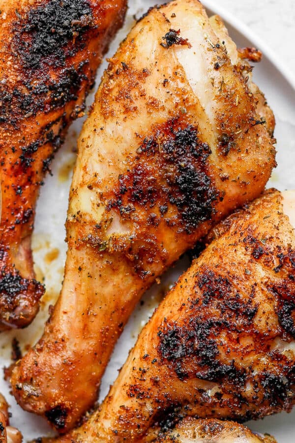 Close-up image of two grilled chicken legs on a plate with a small dish of dip off to the side.
