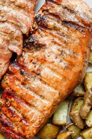 Two grilled pork tenderloins on a plate with potatoes.