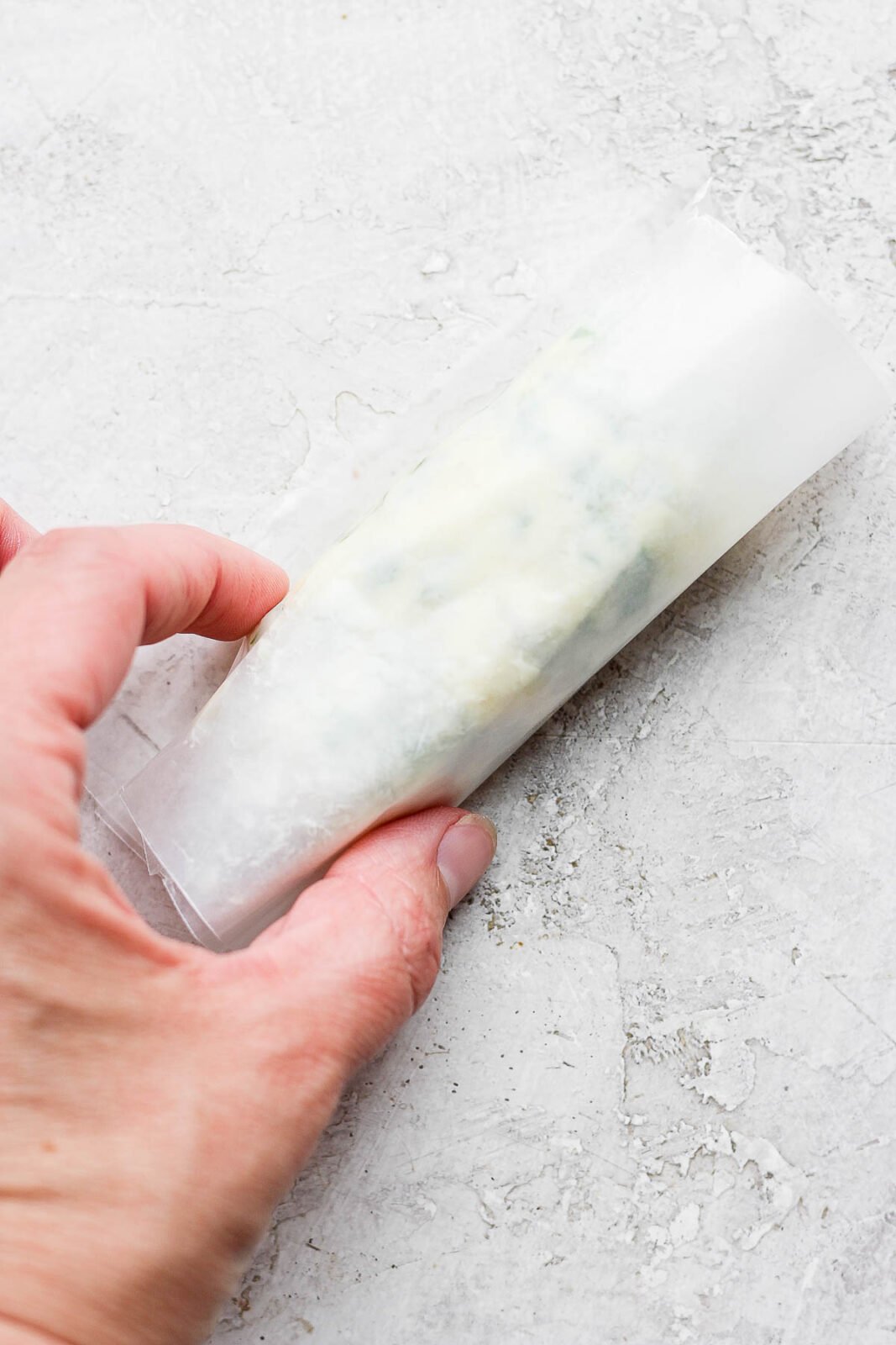 A hand holding herbed butter in wax paper.