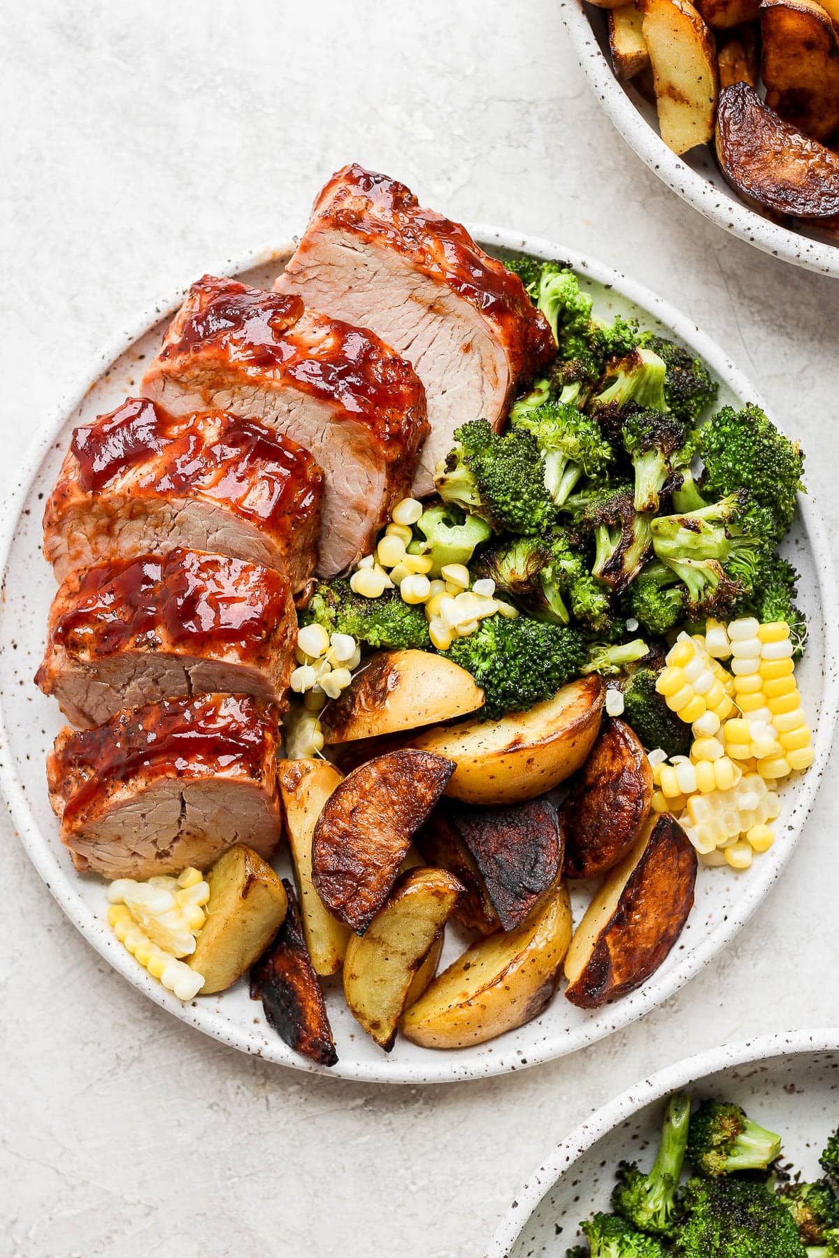 Plate of grilled pork tenderloin with grilled broccoli, corn and potato wedges. 