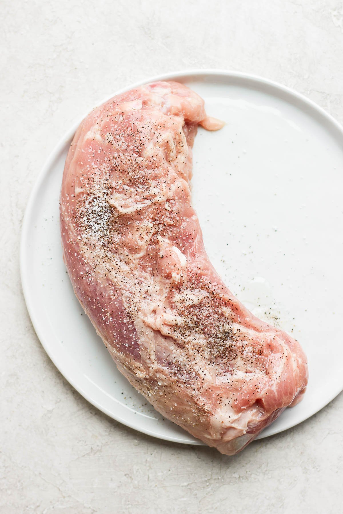 Pork tenderloin on a plate seasoned with salt and pepper. 