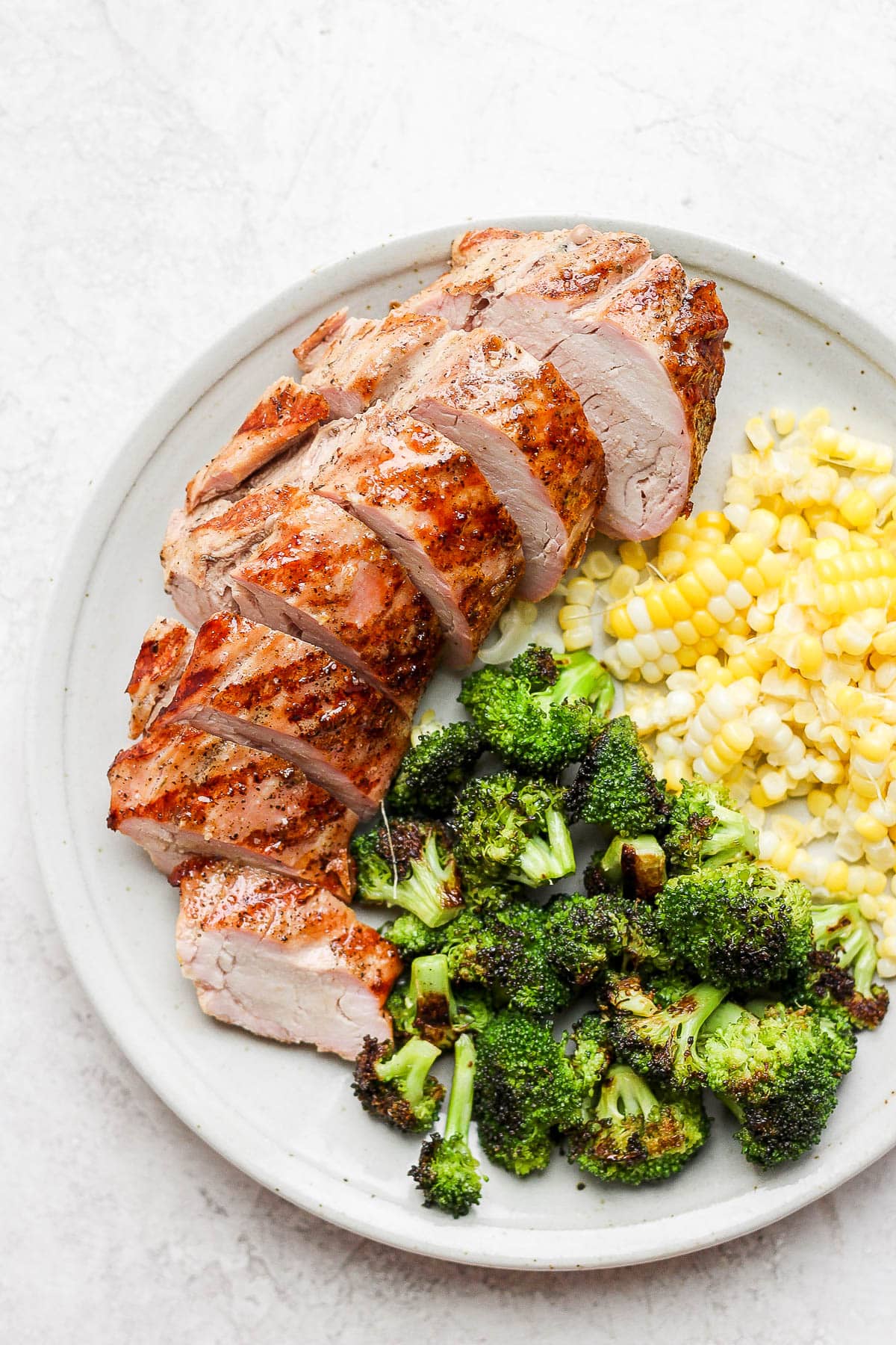 A plate of grilled pork tenderloin, sliced, with corn and broccoli.