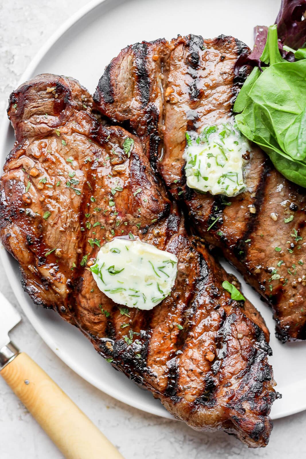 Two steaks with herbed butter on top on a plate. 