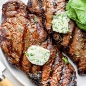 Two grilled steaks with herbed butter on top.