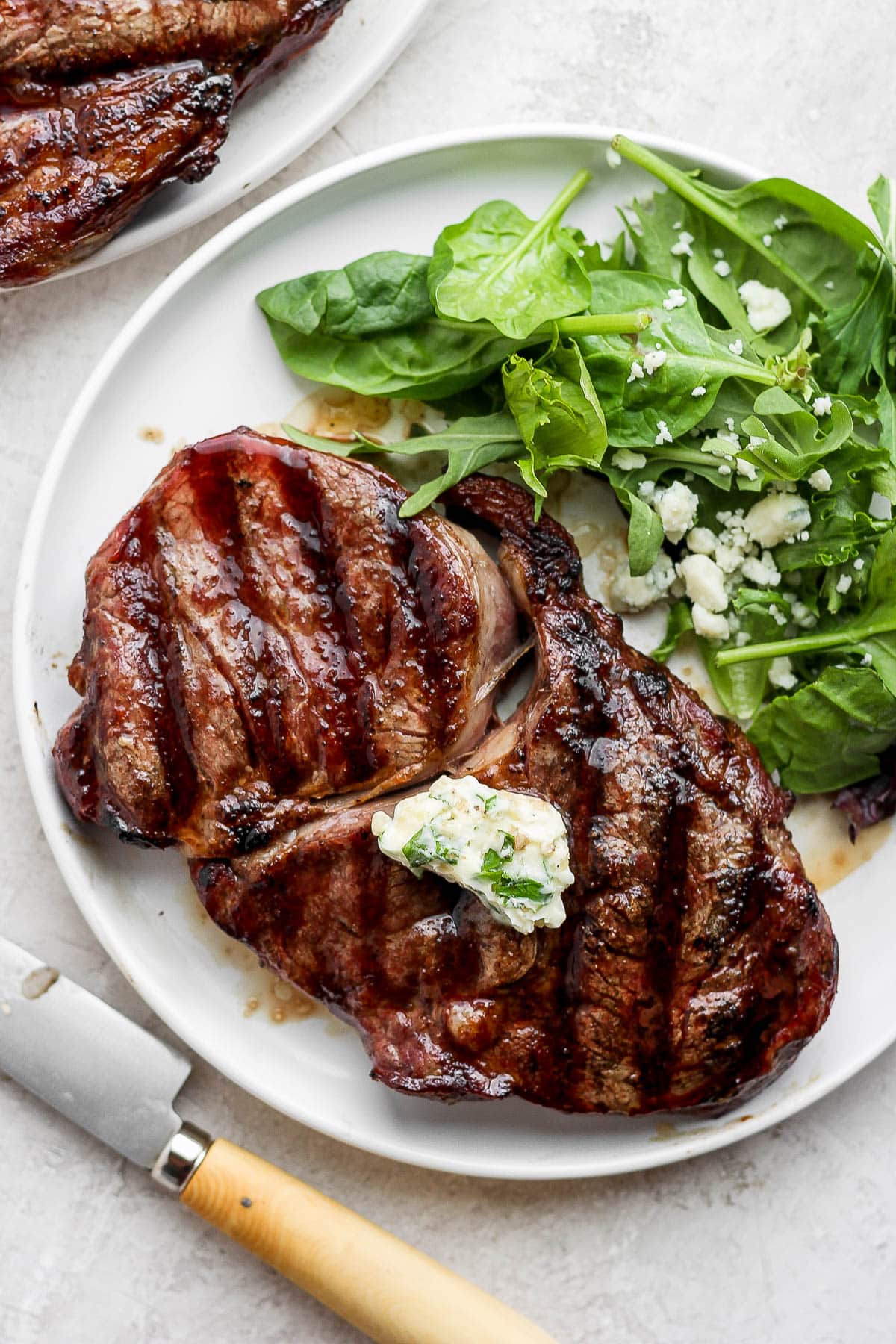 Two grilled filet mignons on a plate with lettuce and blue cheese crumbles. 