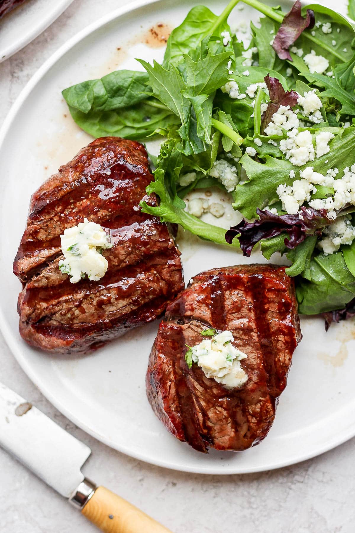 A plate with two grilled steaks and a salad. Steaks are topped with herbed butter.