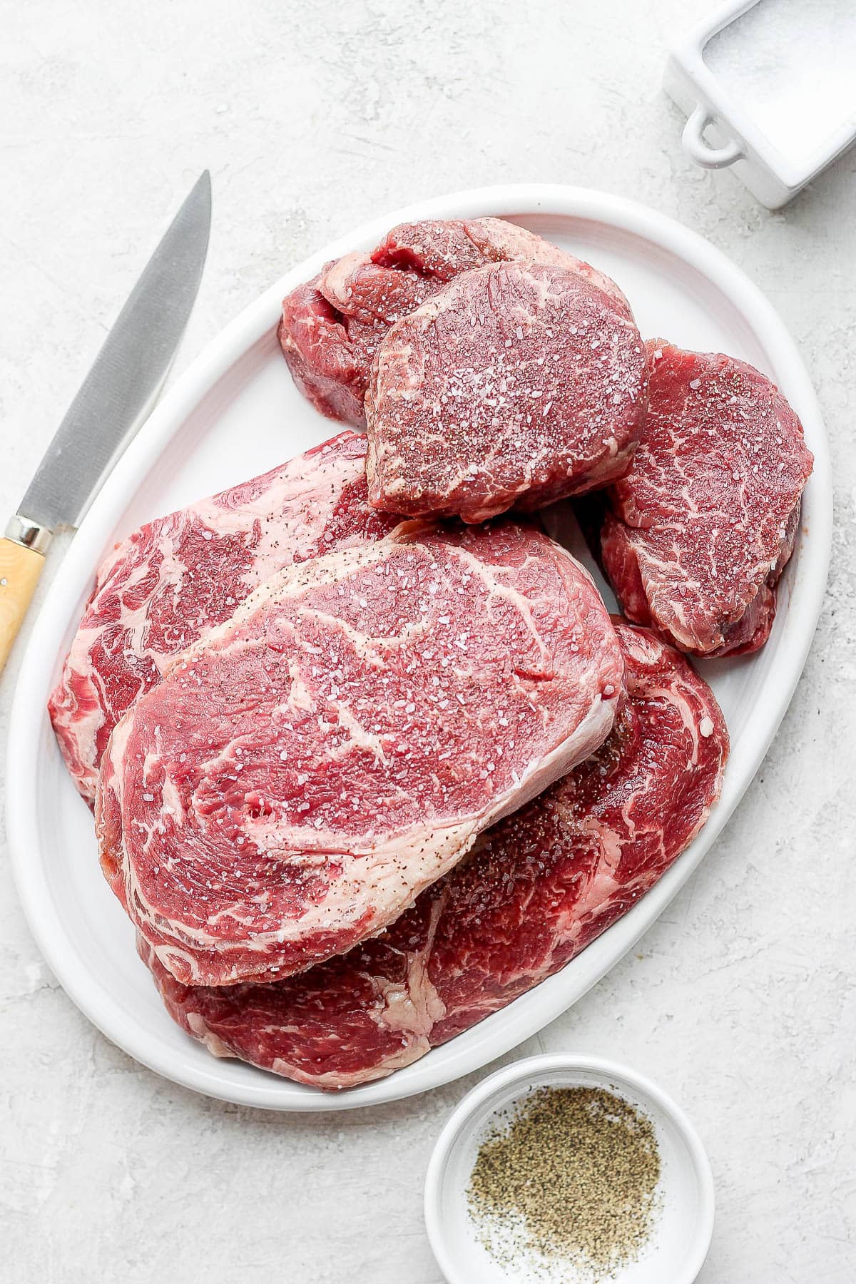 A platter of steaks seasoned with salt and pepper. 