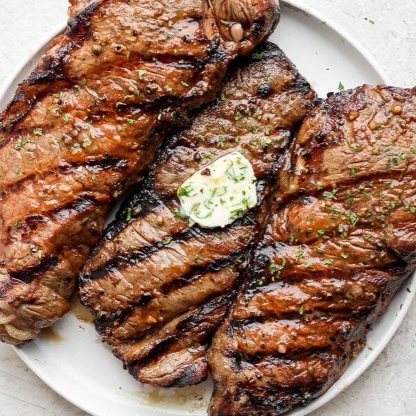 A plate of 3 grilled steaks with herbed butter on top of the middle one.