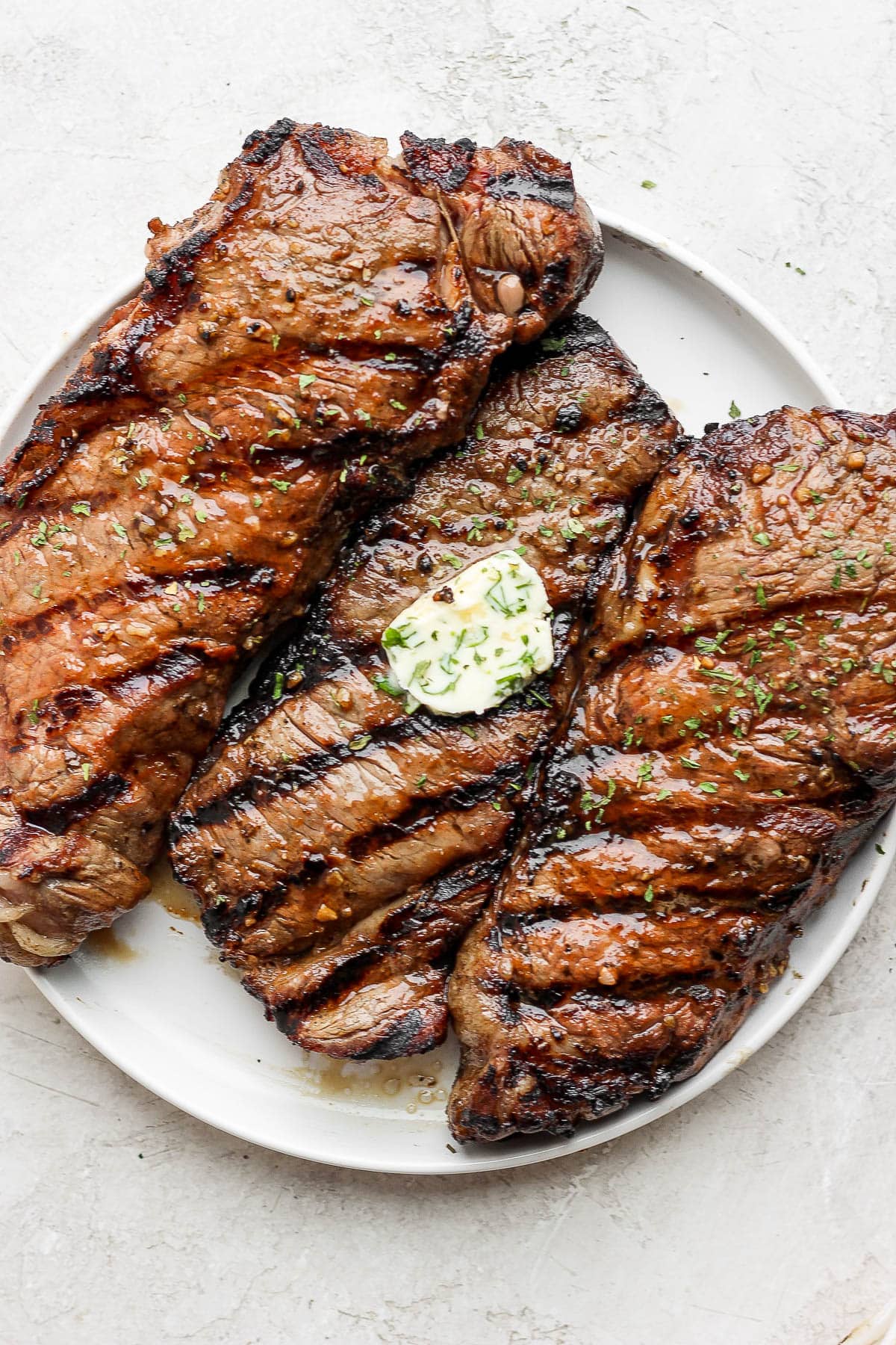Three steaks on a plate, the middle steak has herbed butter on top. 